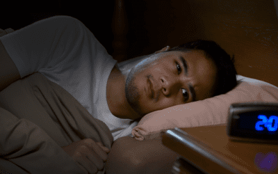 A man lying in bed awake staring at an alarm clock reading 2:04am