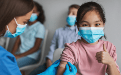 A child wearing a mask giving a thumbs up after having received a vaccine from a doctor.
