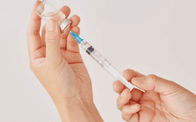 Hands holding a vaccine vial with syringe inserted