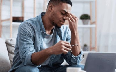 A man pinching the bridge of his nose while holding his glasses in the other hand exhibiting exhaustion