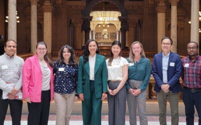 Nine scientists stand with an Indiana State Senator in a gallery of the Indiana Statehouse