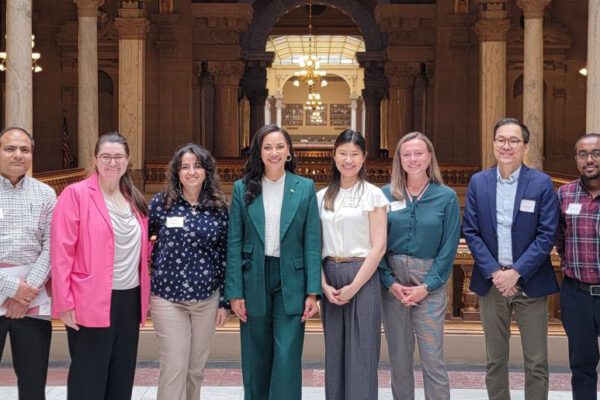Nine scientists stand with an Indiana State Senator in a gallery of the Indiana Statehouse
