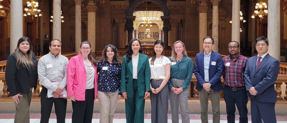 Nine scientists stand with an Indiana State Senator in a gallery of the Indiana Statehouse