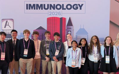 Group shot of 14 high school students and their teacher in front of the selfie backdrop of Boston's skyline at IMMUNOLOGY2026™