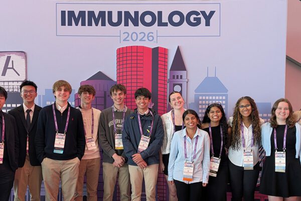 Group shot of 14 high school students and their teacher in front of the selfie backdrop of Boston's skyline at IMMUNOLOGY2026™