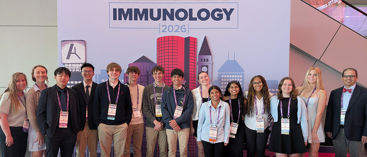 Group shot of 14 high school students and their teacher in front of the selfie backdrop of Boston's skyline at IMMUNOLOGY2026™