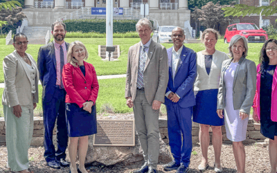 AAI leaders and staff poses on a sunny day by a plaque on the NIH campus.