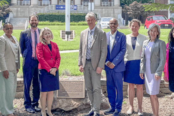 AAI leaders and staff poses on a sunny day by a plaque on the NIH campus.