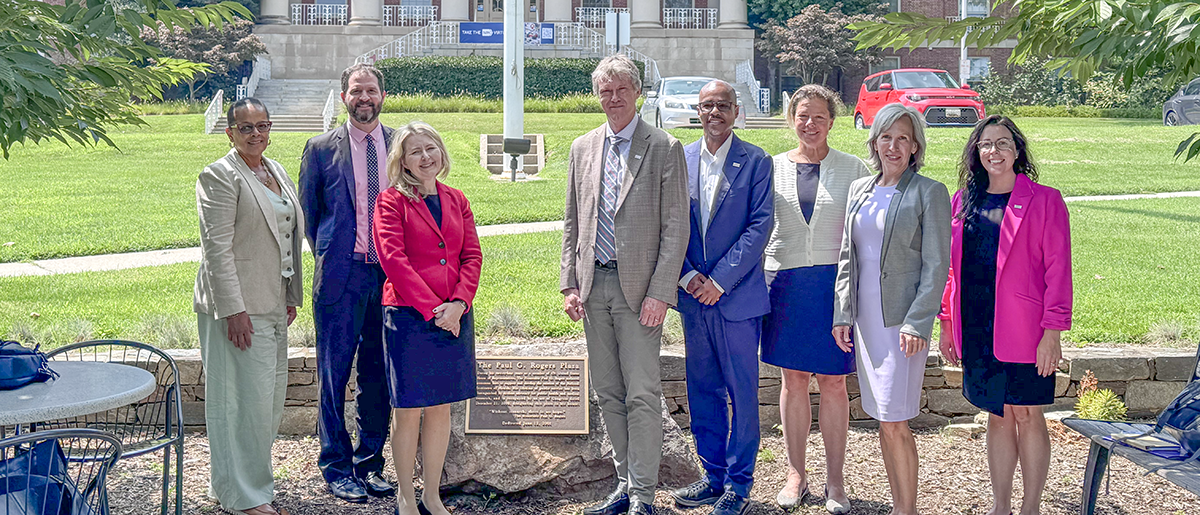 AAI leaders and staff poses on a sunny day by a plaque on the NIH campus.