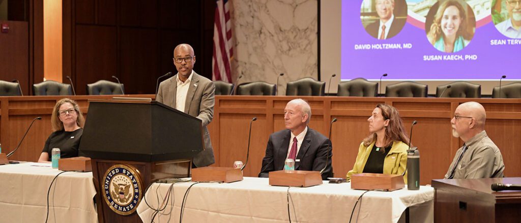 Marion Pepper, Avery August, David Holtzman, Susan Kaech, and Sean Terwilliger sit at a panel table. Dr. August is speaking at the lectern.
